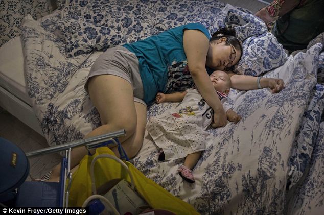 Room for two: A woman curls up with her baby on a rather ruffled bed in the cool, air-conditioned IKEA store