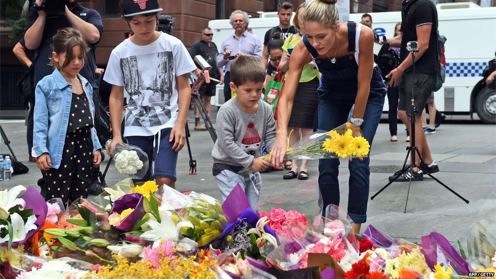 Children lay flowers at the scene of a dramatic siege which left two hostages dead in Sydney