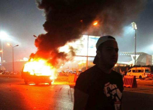 A soccer fan is seen near a police car, which was set on fire by fireworks, during clashes between soccer fans and security forces in front of a stadium on the outskirts of Cairo February 8, 2015. REUTERS-Al Youm Al Saabi Newspaper