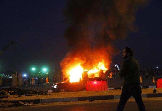 A soccer fan is seen near a police car, which was set on fire by fireworks, during clashes between soccer fans and security forces in front of a stadium on the outskirts of Cairo February 8, 2015. REUTERS-Stringer