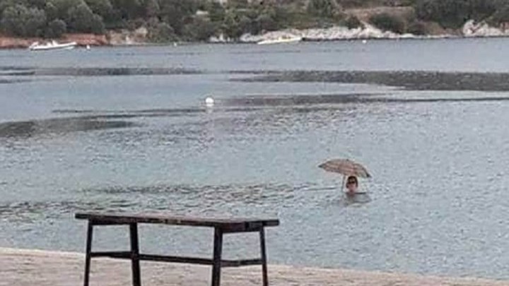Ούτε η βροχή δεν την πτοεί – Μπήκε στη θάλασσα με… ομπρέλα και έγινε viral – ΦΩΤΟ