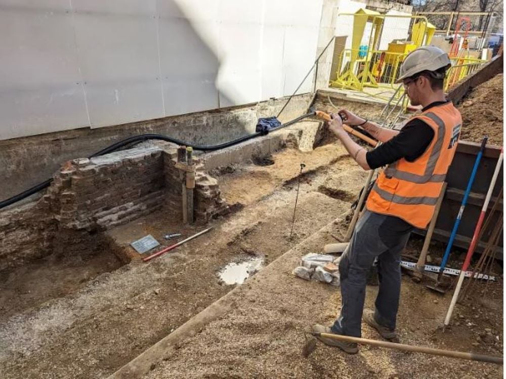 An archaeologist photographs part of the excavation.  It appears to be part of a post-medieval wall.