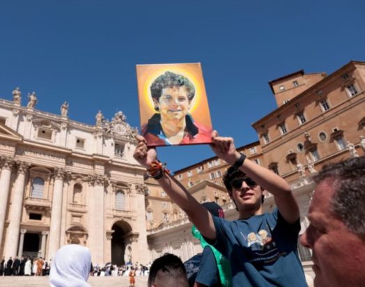 Ένα άτομο κρατά έναν πίνακα του Κάρλο Ακούτις, ο οποίος σύντομα θα αγιοποιηθεί.