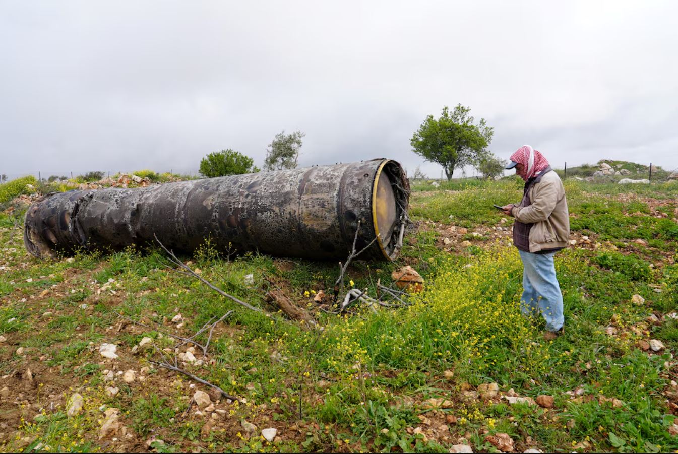Ένα άτομο στέκεται δίπλα στα απομεινάρια ενός ιρανικού πυραύλου, αφότου το Ιράν εξαπέλυσε μπαράζ πυραύλων προς το Ισραήλ, εν μέσω της αμερικανο-ισραηλινής σύγκρουσης με το Ιράν, στο χωριό Μπεϊτίν κοντά στη Ραμάλα, στην κατεχόμενη από το Ισραήλ Δυτική Όχθη, στις 26 Μαρτίου 2026. REUTERS/Ali Sawafta