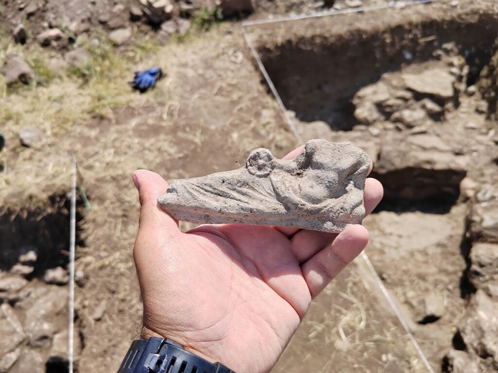 Διακοσμητικό εξάρτημα από κλίνη (ανάκλιντρο συμποσίου) που απεικονίζει μια θεότητα να κρατά φιάλη. Η φωτογραφία παραχωρήθηκε ευγενικά από τον διευθυντή του έργου, Ντέγιαν Γκιόργκιεφσκι (Dejan Gjorgjievski) 