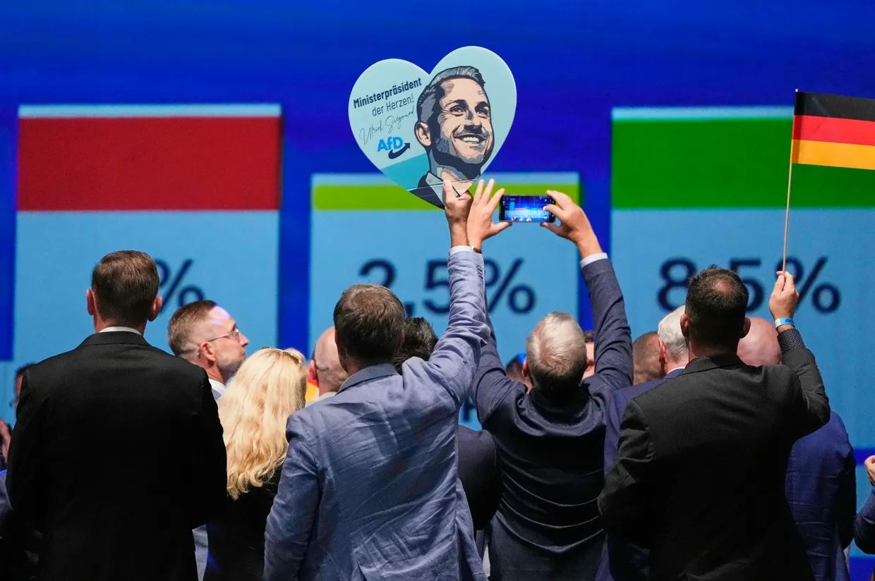 Μέλη του AfD πανηγυρίζουν κρατώντας πλακάτ με τον κορυφαίο υποψήφιο του κόμματος, Ούλριχ Ζίγκμουντ, μετά την ανακοίνωση των πρώτων αποτελεσμάτων στις περιφερειακές εκλογές της Σαξονίας-Άνχαλτ, στο Μαγδεμβούργο της ανατολικής Γερμανίας, την Κυριακή 6 Σεπτεμβρίου 2026. Φωτογραφία: AP / Matthias Schrader