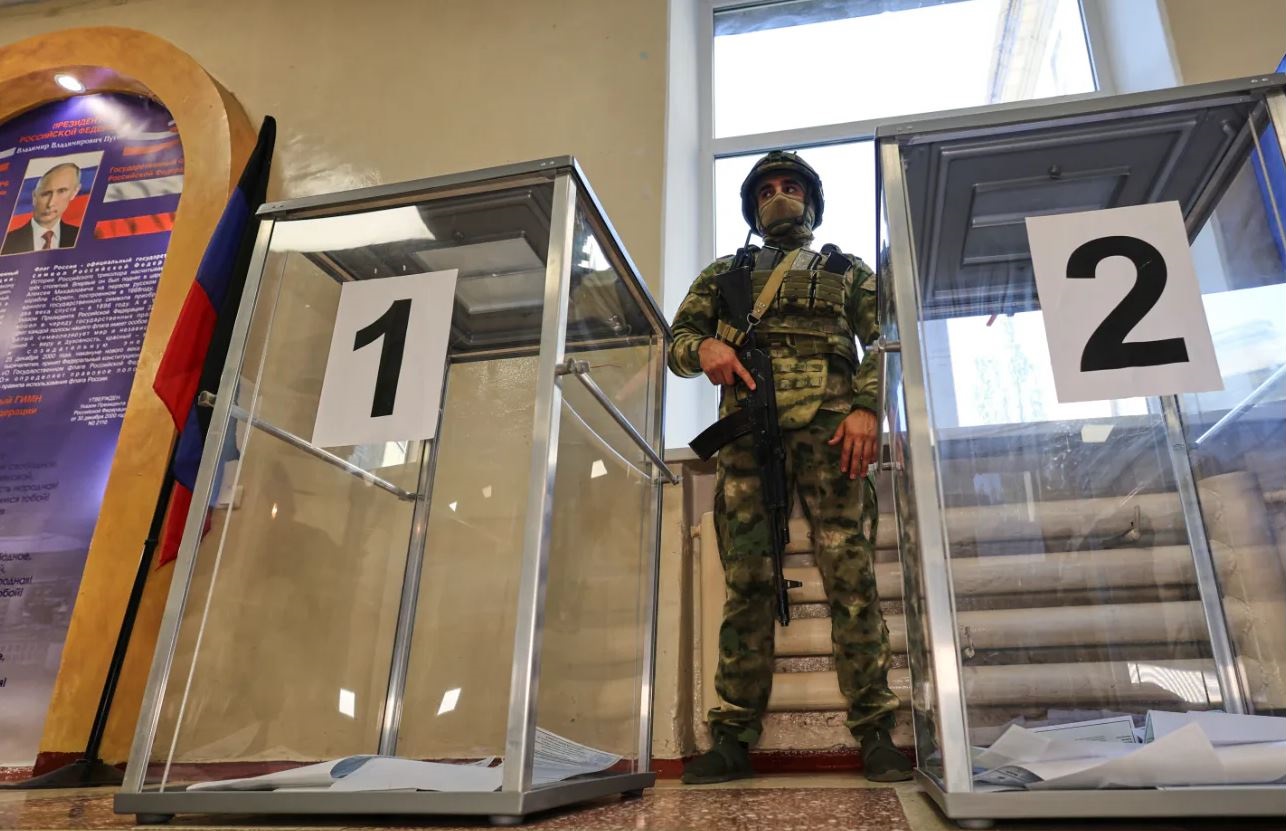 Ένοπλος φρουρός στέκεται ανάμεσα σε κάλπες σε εκλογικό τμήμα κατά τη διάρκεια των ρωσικών βουλευτικών εκλογών σε κατεχόμενη περιοχή της Ουκρανίας. Φωτογραφία: AP