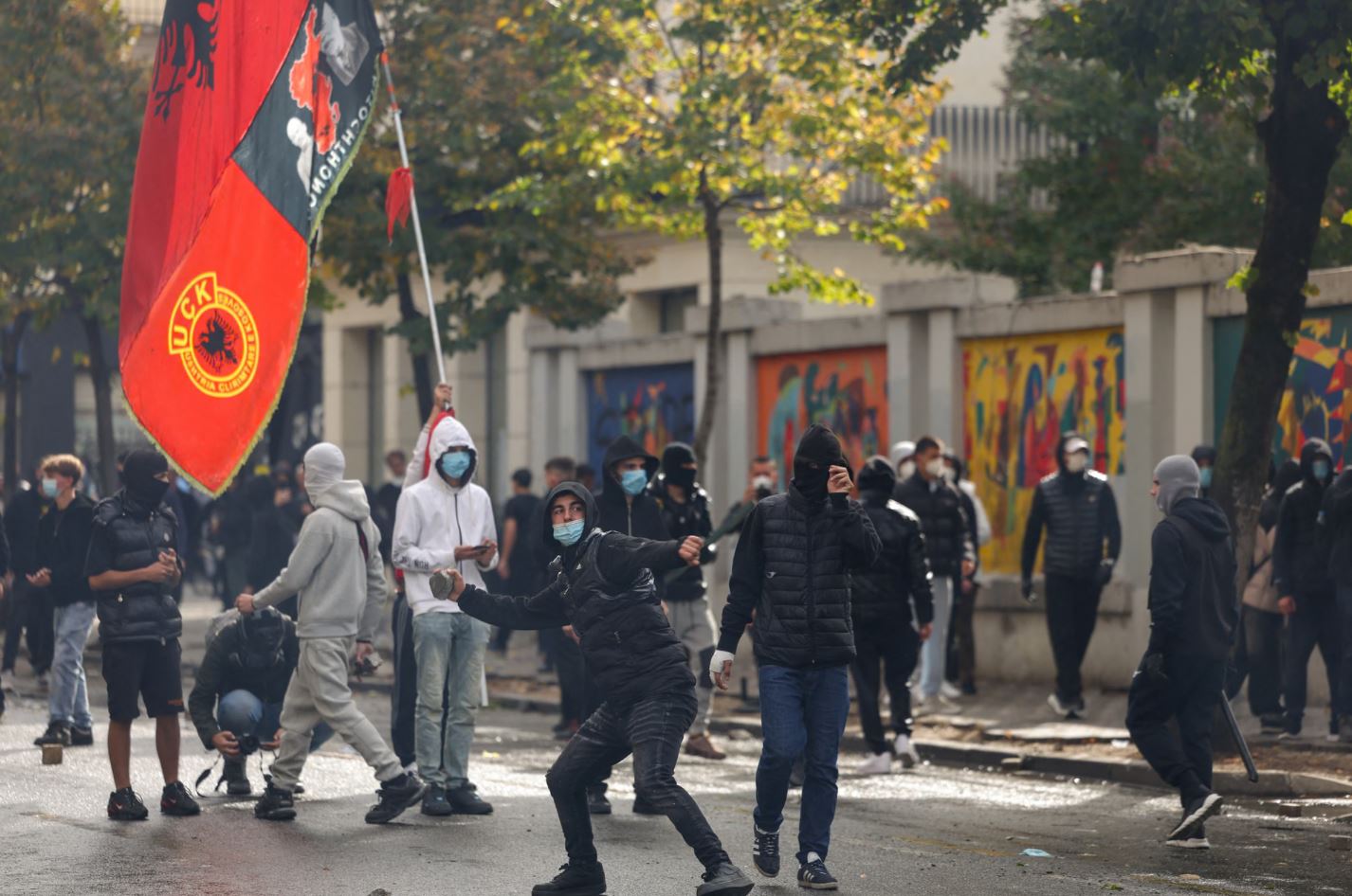 Κουκουλοφόρος διαδηλωτής ετοιμάζεται να εκτοξεύσει αντικείμενο κατά τη διάρκεια των αντικυβερνητικών κινητοποιήσεων στα Τίρανα της Αλβανίας, με τη σημαία του UÇK (Απελευθερωτικού Στρατού του Κοσσυφοπεδίου) να κυματίζει πίσω του. (Φωτογραφία: Florion Goga/Reuters)