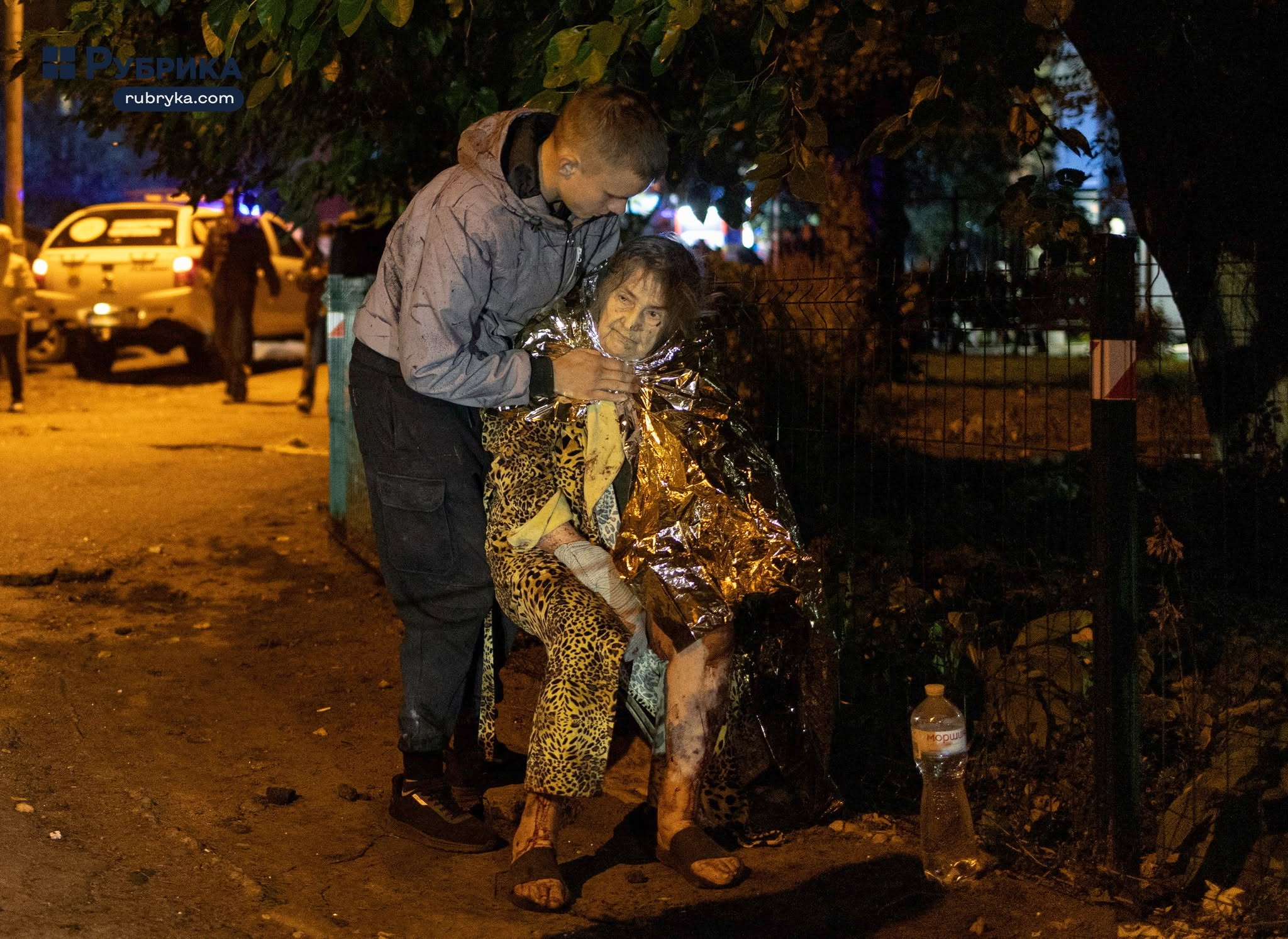 Τραυματισμένη ηλικιωμένη γυναίκα, τυλιγμένη με ισοθερμική κουβέρτα, δέχεται βοήθεια από νεαρό άνδρα μετά τη ρωσική επίθεση στο Κίεβο της Ουκρανίας, την Τρίτη (13/10). (Πηγή: Rubryka / Nick Tymchenko)