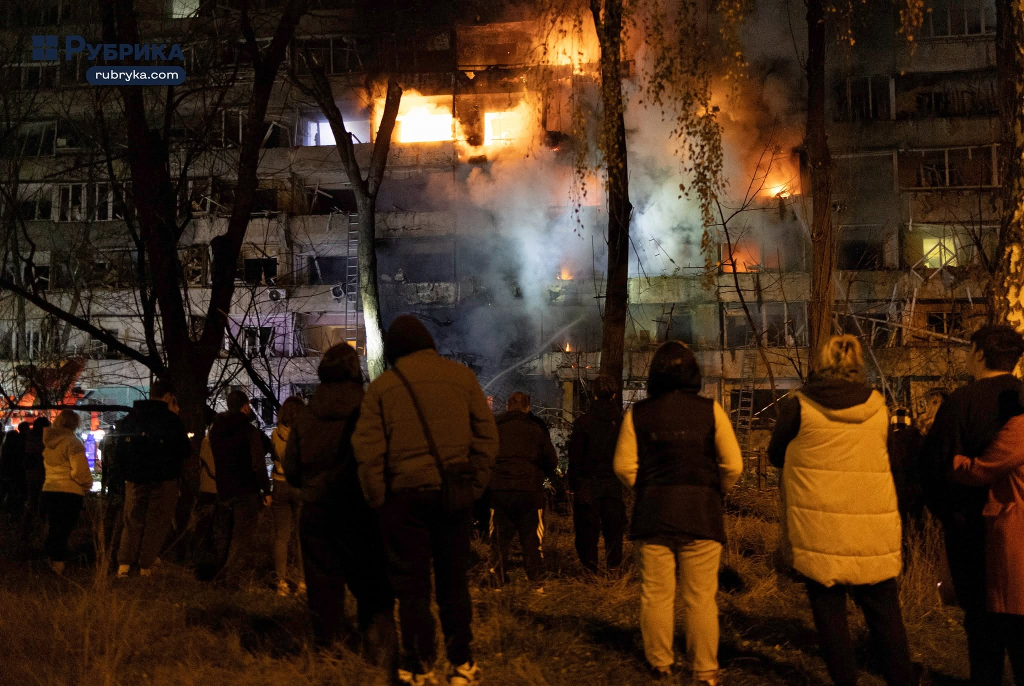 Κάτοικοι παρακολουθούν πολυκατοικία να έχει τυλιχθεί στις φλόγες, με πυκνούς καπνούς να υψώνονται από τους ορόφους της, μετά τη ρωσική επίθεση στο Κίεβο, την Τρίτη (13/10). Σύμφωνα με τις τοπικές αναφορές, τρεις άνθρωποι σκοτώθηκαν και 22 τραυματίστηκαν στην ουκρανική πρωτεύουσα. (Πηγή: Rubryka / Nick Tymchenko)